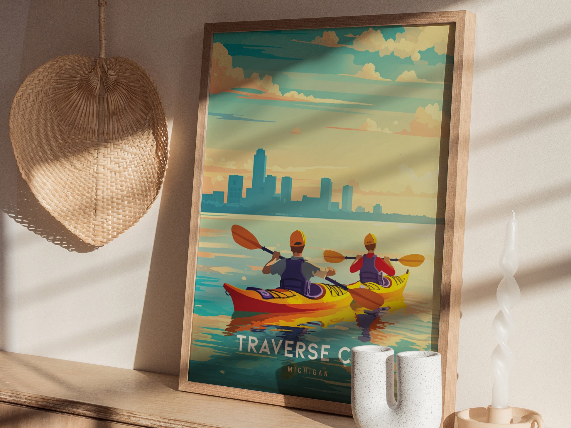 A framed poster depicting two kayakers on a calm bay with a city skyline at sunset. The poster is propped against a wall with a woven hat and decorative items.