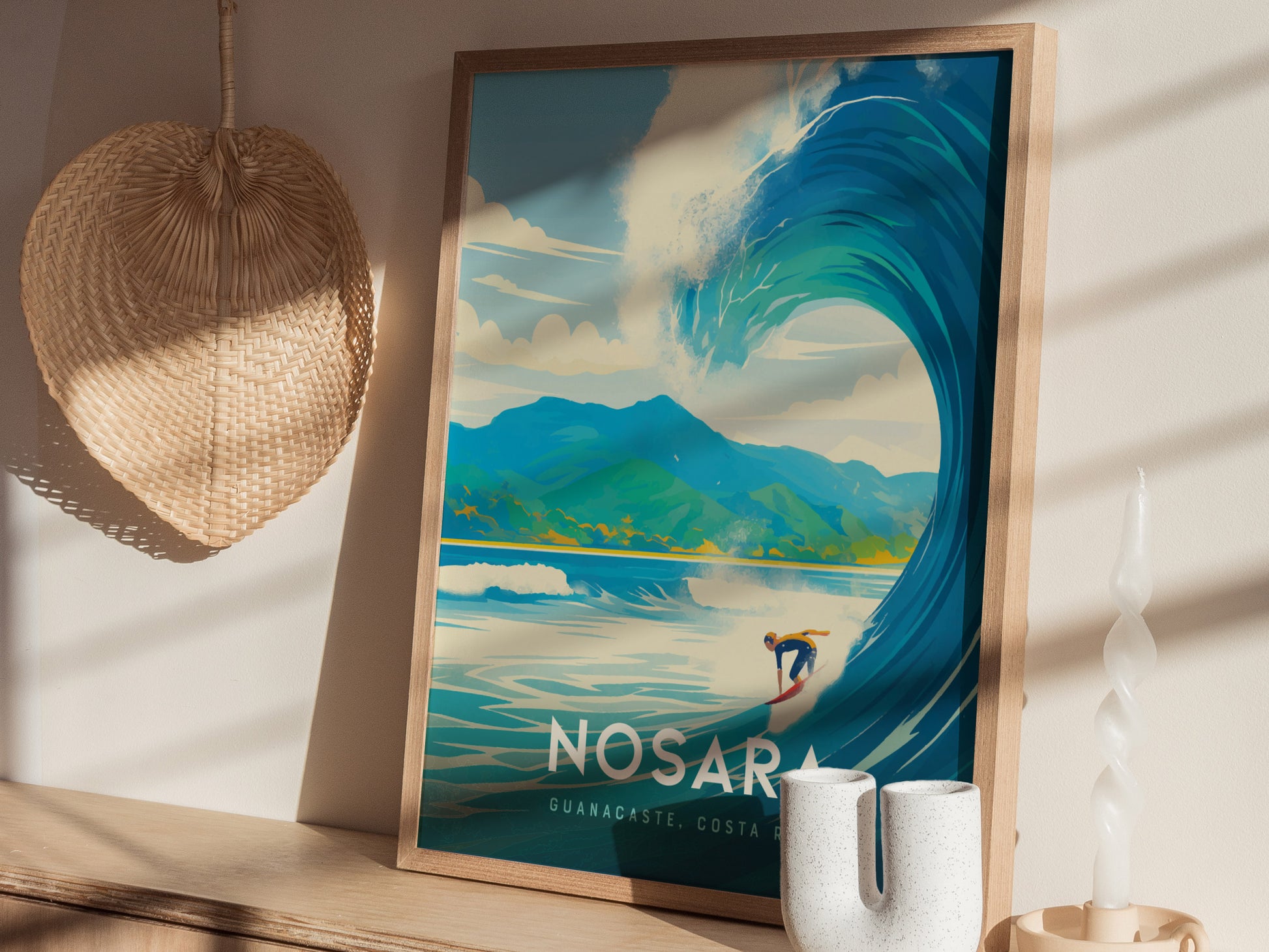 A framed poster of a surfer on a large wave with mountains in the background sits on a wooden shelf. A woven basket and twisted candle are nearby, casting shadows.
