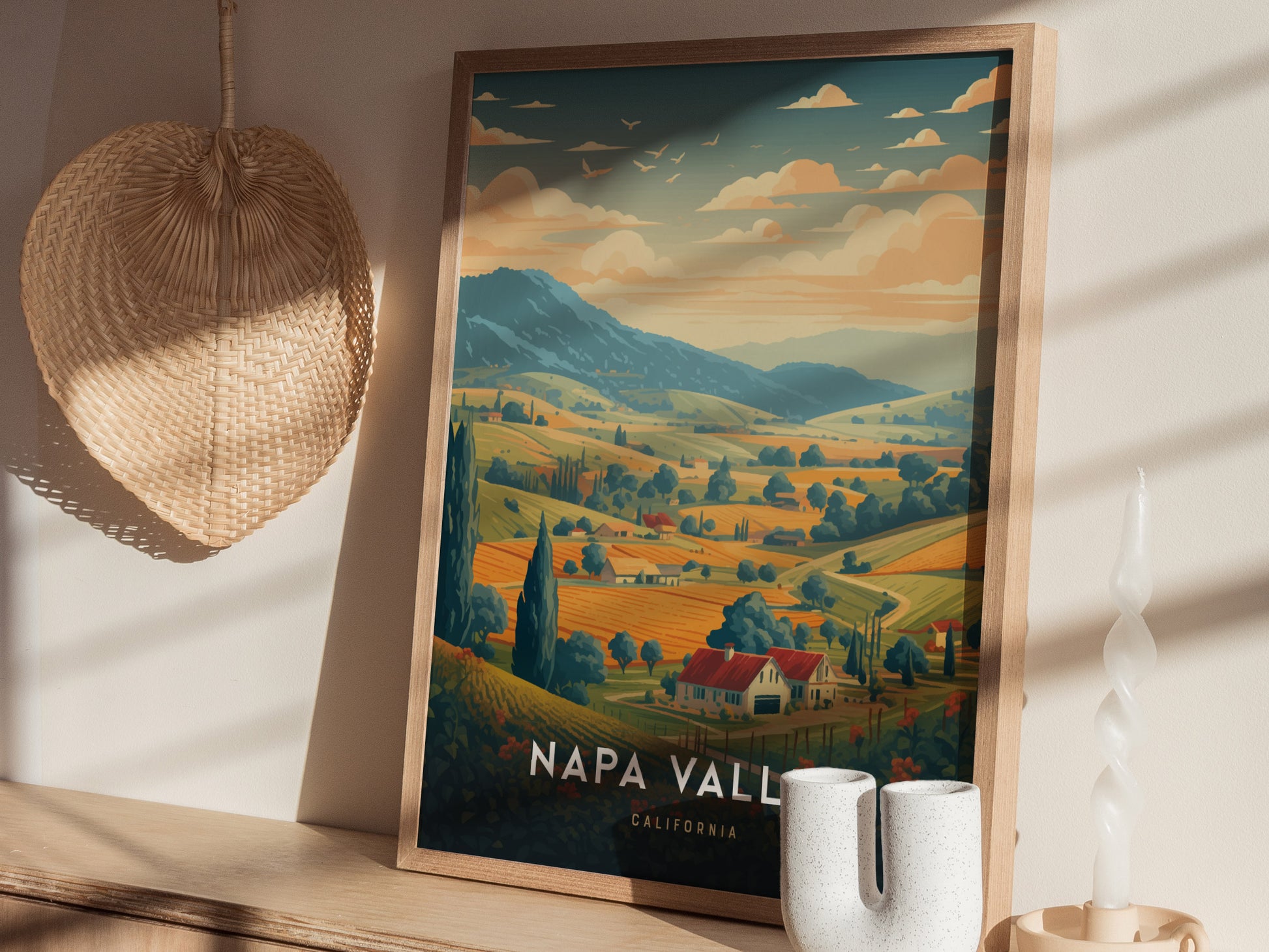 Framed Napa Valley travel poster depicting rolling vineyards and hills under a warm sky, placed on a wooden shelf with a woven basket and decorative candle.