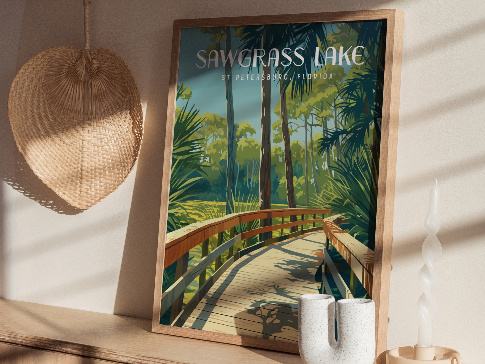 A framed poster of Sawgrass Lake Park with a wooden boardwalk and lush greenery is displayed on a shelf, accompanied by a wicker fan and decorative items.