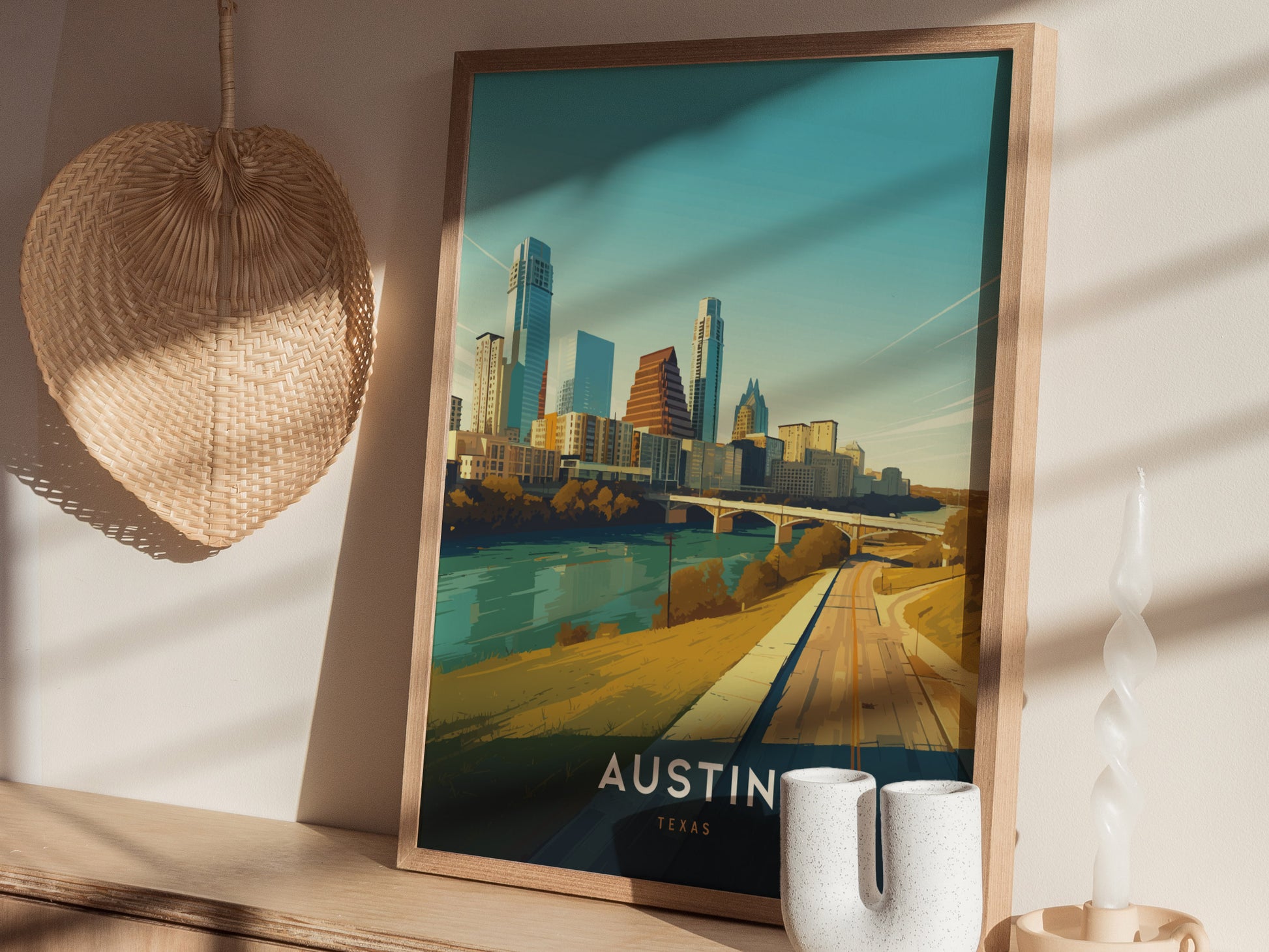A framed Austin, Texas skyline poster sits on a wooden shelf with a woven wall decoration and a modern ceramic candle holder nearby, illuminated by soft sunlight.