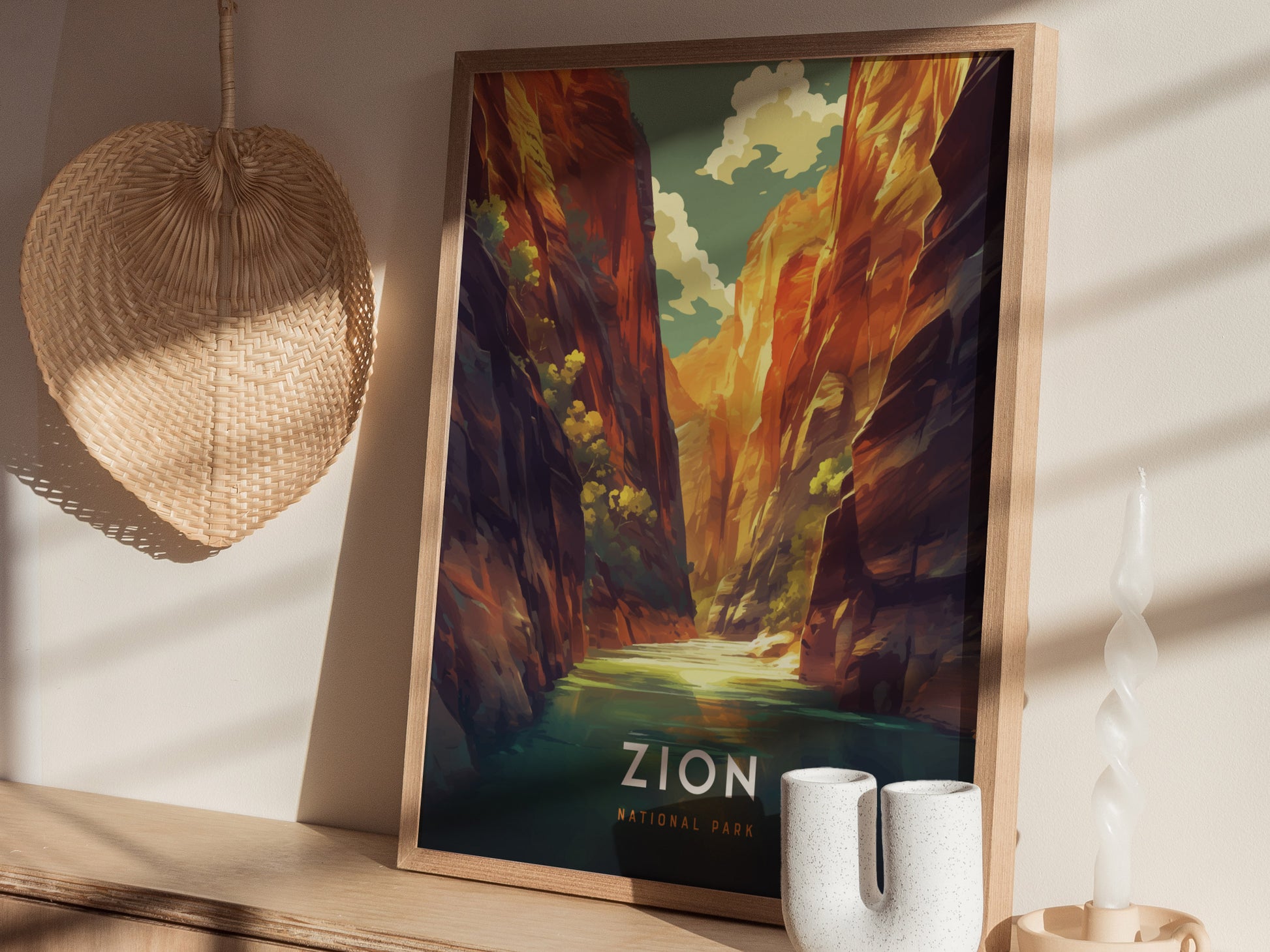 A framed poster of Zion National Park, depicting colorful canyon cliffs and a river, sits on a wooden surface with a woven fan and a twisted candle nearby.