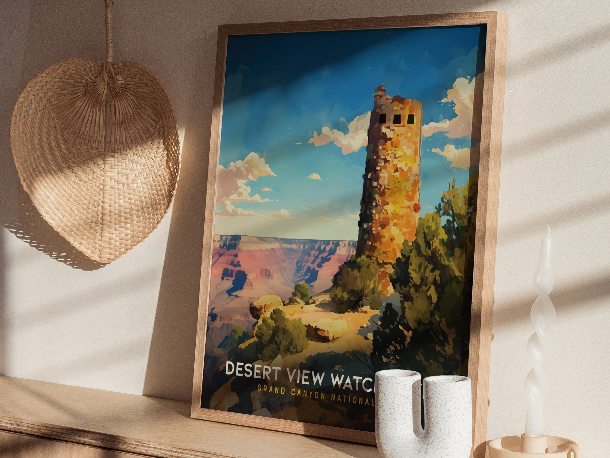A framed poster of the Desert View Watchtower at the Grand Canyon is displayed on a wooden shelf, alongside a woven wall decoration and a twisted white candle.