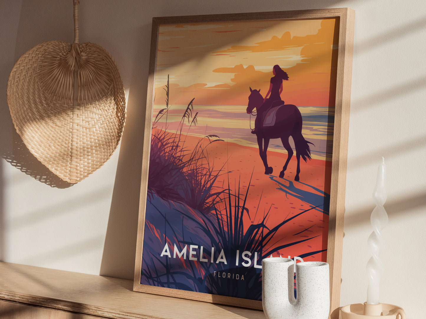 A framed Amelia Island poster depicting a woman riding a horse along the beach at sunset, with warm golden hues and sea oats.