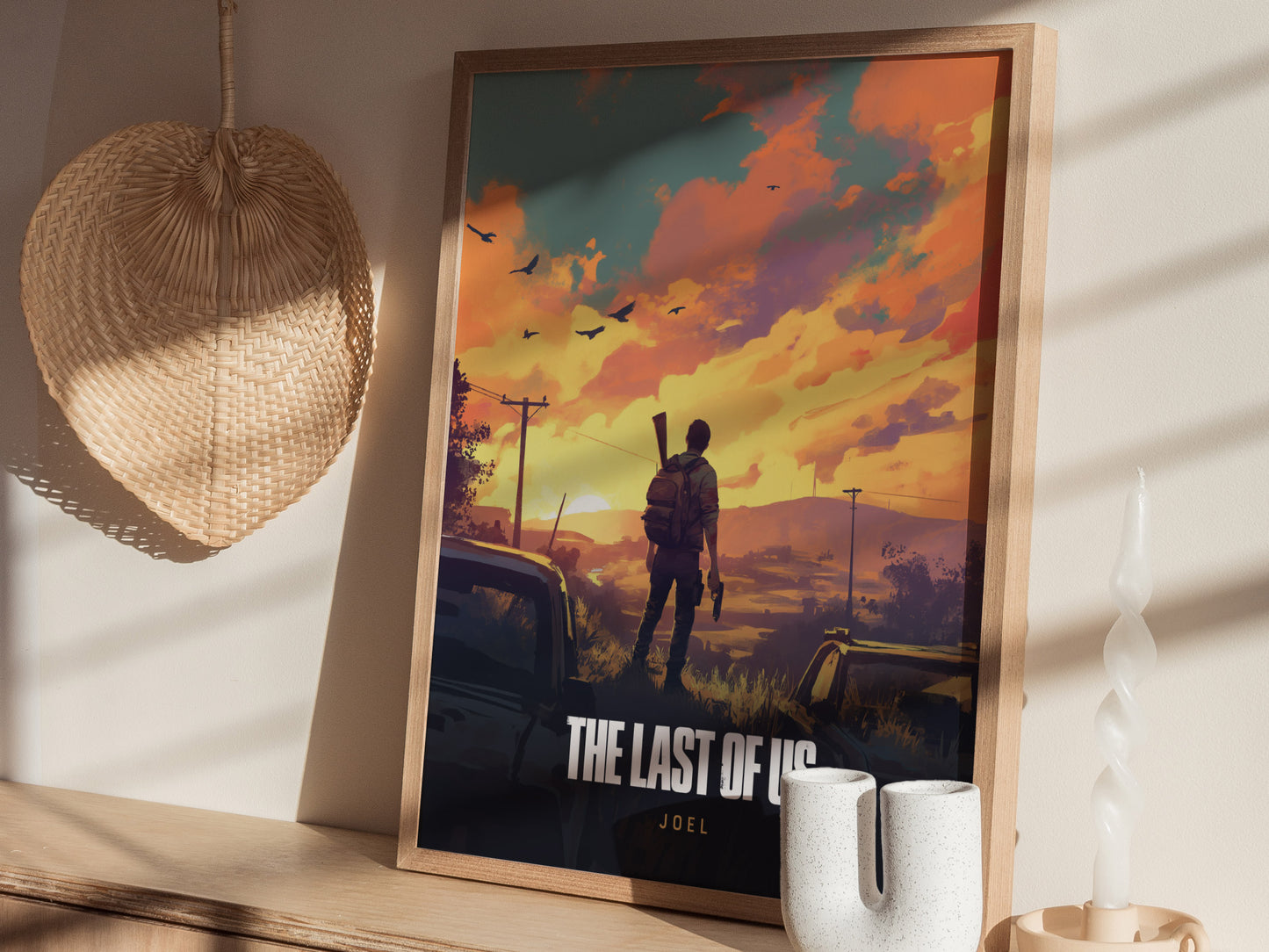 A framed poster of The Last of Us featuring a silhouette of a man with a backpack against a vibrant sunset. Its placed on a shelf beside a wicker fan.