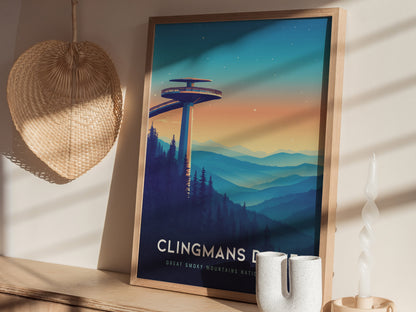 A framed Clingmans Dome poster sits on a wooden shelf, depicting a colorful mountain landscape with a prominent observation tower. Nearby, a woven basket hangs on the wall and a twisted white candle stands on the shelf.
