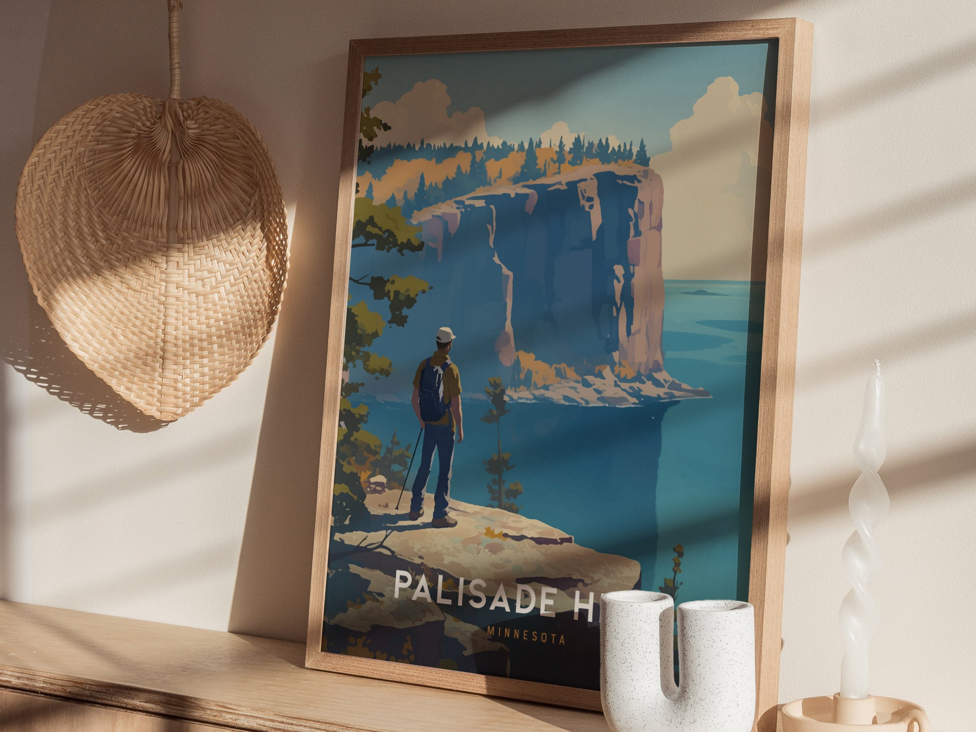 A framed poster of Palisade Head, Minnesota, showing a hiker overlooking dramatic cliffs and Lake Superior. The poster is displayed on a wooden shelf with a woven wall decor.