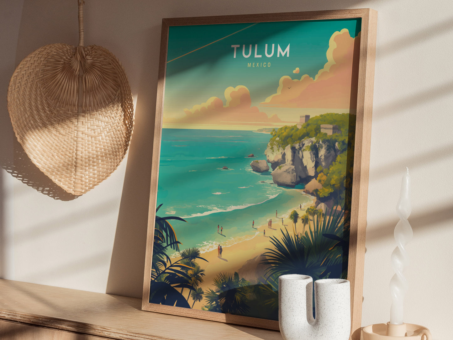 Framed Tulum Mexico poster featuring vibrant turquoise waters and Mayan ruins on a cliff. The scene is set on a wooden shelf with a woven fan and decorative items nearby.