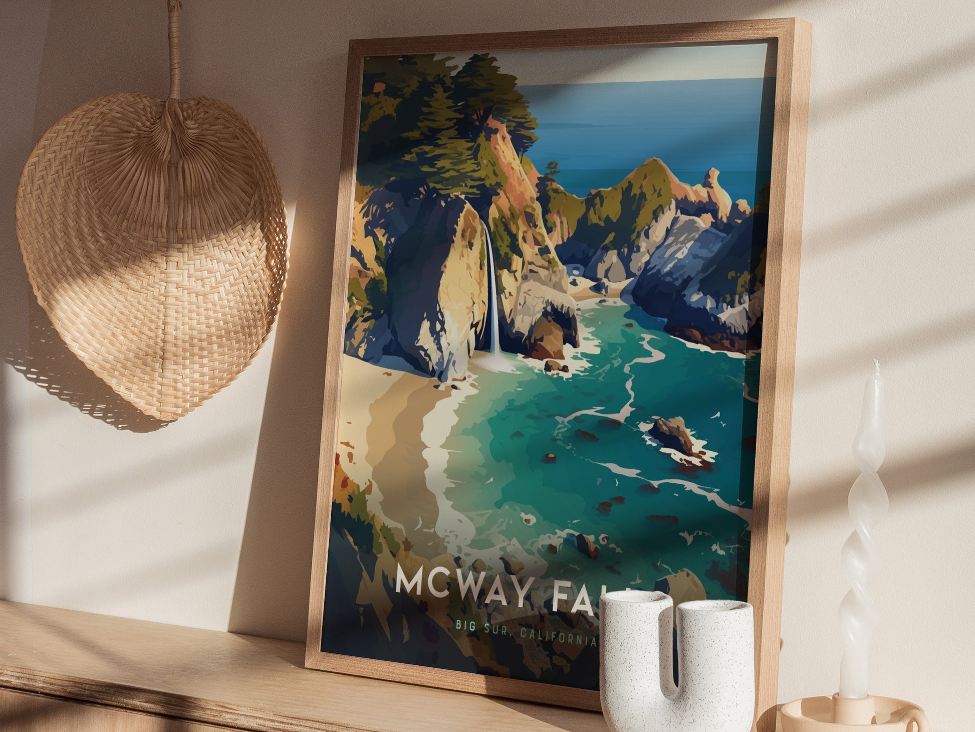 Framed McWay Falls poster depicting a vibrant coastal scene with turquoise waters, cliffs, and a waterfall. It rests on a wooden surface beside a woven basket and a decorative candle.