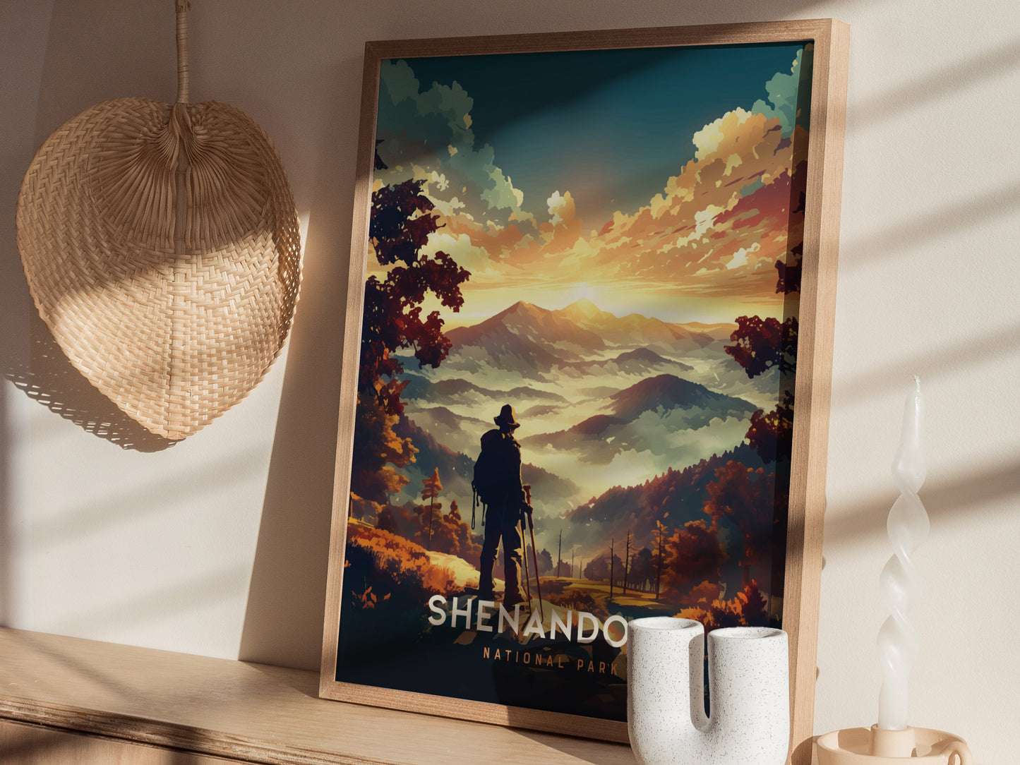 A framed Shenandoah National Park poster features a silhouette of a hiker overlooking vibrant mountains at sunset. Nearby are a woven fan, twisted candle, and ceramic vase.