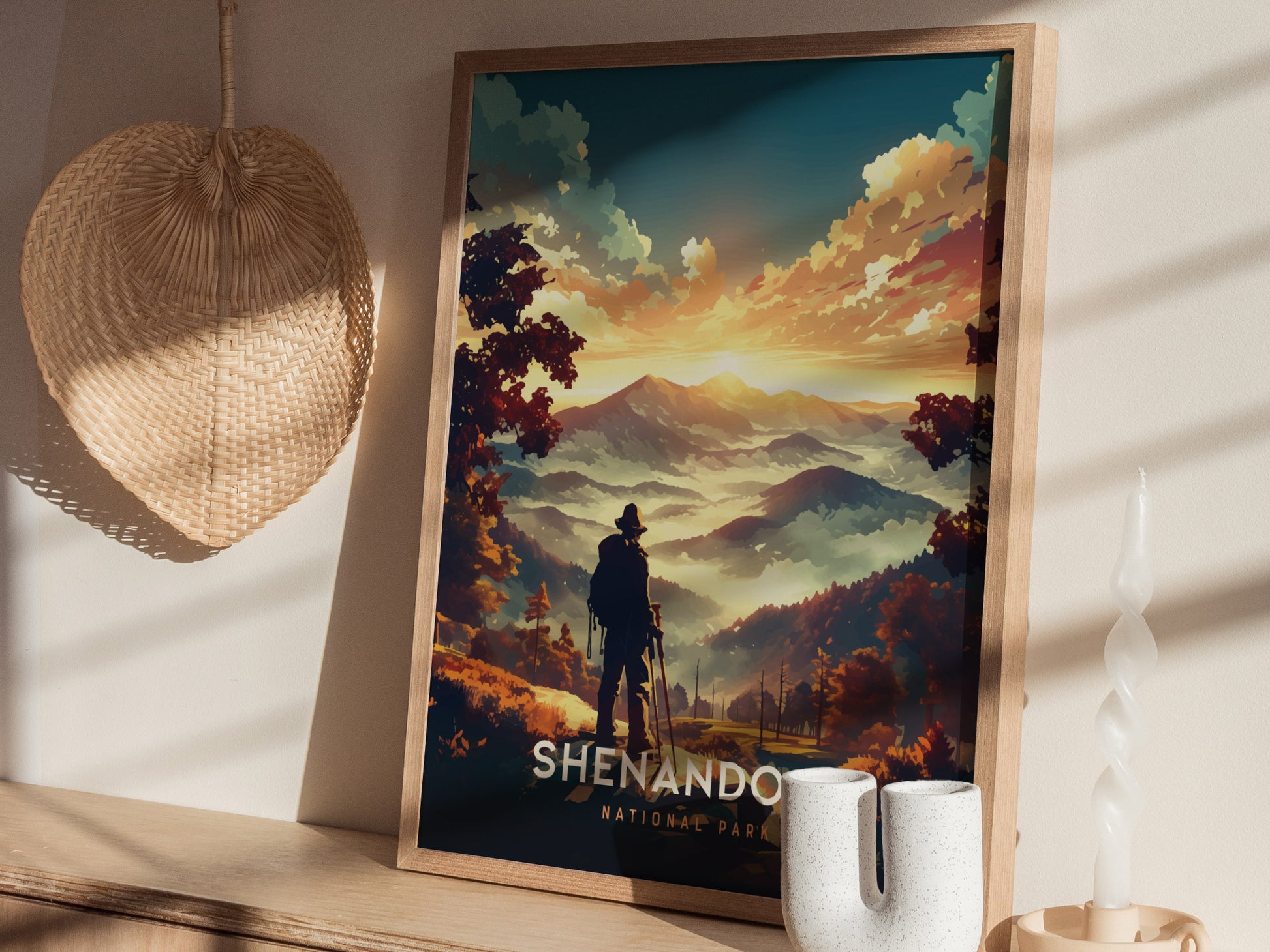 A framed Shenandoah National Park poster features a silhouette of a hiker overlooking vibrant mountains at sunset. Nearby are a woven fan, twisted candle, and ceramic vase.