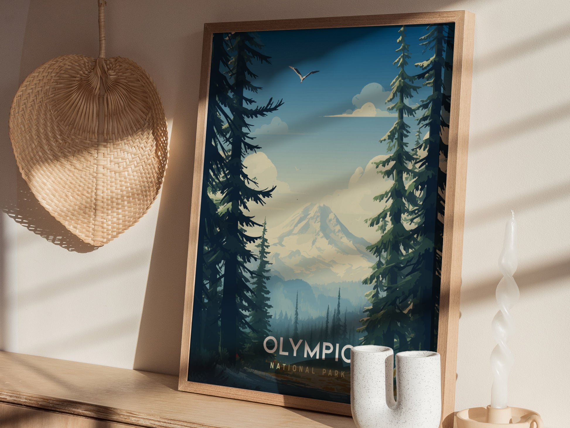 A framed Olympic National Park poster featuring a mountain landscape with tall evergreen trees and a bird in the sky. The poster is displayed on a wooden shelf next to.