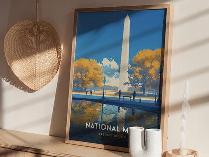 A framed poster of the Washington Monument reflecting in water, set against an autumn backdrop with yellow trees, sits on a wooden shelf next to a woven wall decoration.