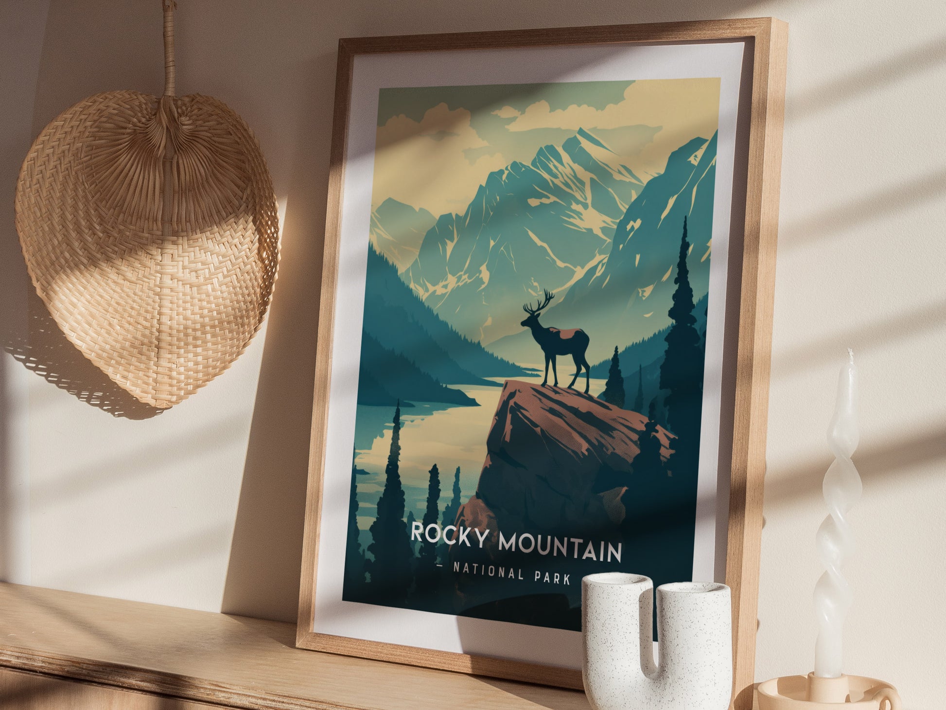 A framed poster of Rocky Mountain National Park features a minimalist design with an elk on a cliff, surrounded by mountains and lakes.