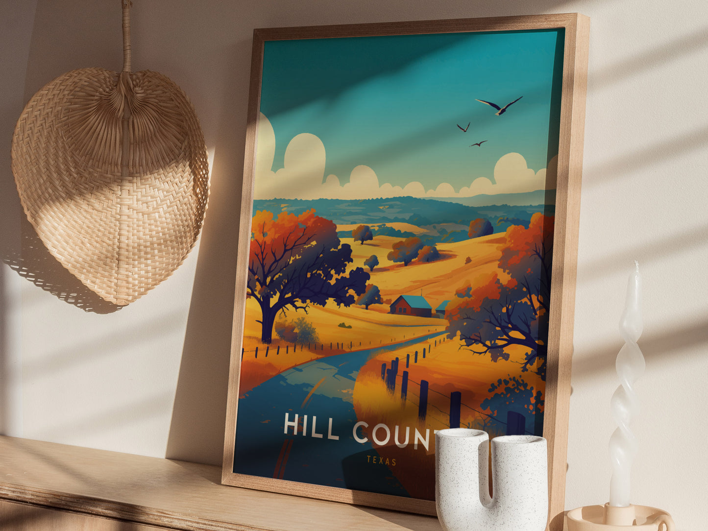 A framed poster depicting a vibrant landscape of rolling hills and trees under a blue sky, titled Hill Country Texas, is displayed on a sunlit shelf with decorative items.