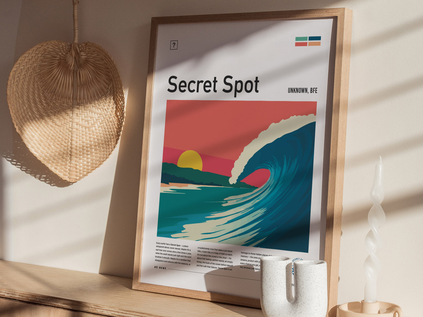 A framed poster titled Secret Spot features a vibrant illustration of a crashing wave against a backdrop of pastel skies and a setting sun. The artwork is displayed on a wooden shelf, accompanied by a woven basket and decorative items.