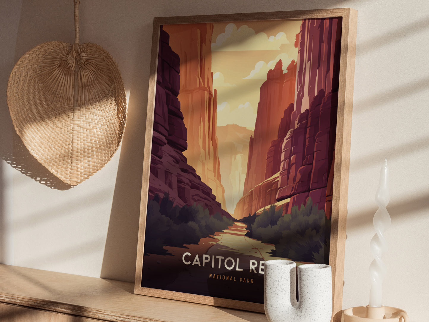 A framed poster of Capitol Reef National Park with red rock canyons is displayed on a wooden surface, accompanied by a woven fan.