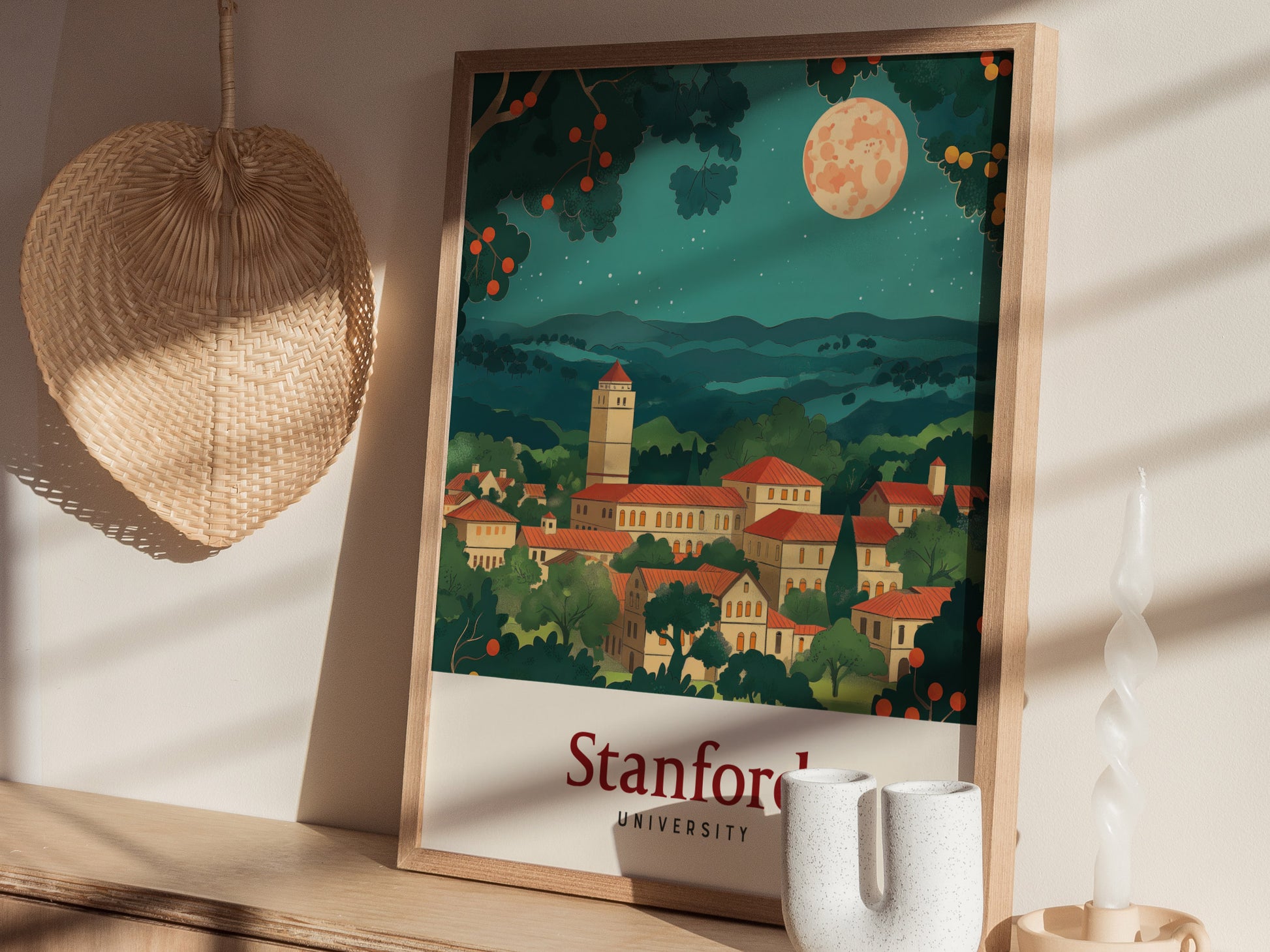 A framed Stanford University poster with a vintage style depicts a picturesque campus under a starry night sky. Its displayed alongside a woven wall decoration and a ceramic vase.