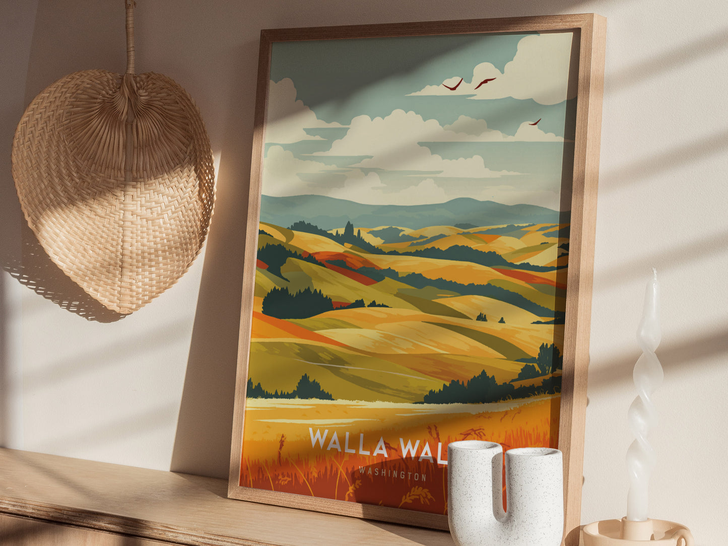 A framed poster depicting colorful rolling hills and vineyards rests on a wooden surface, next to a woven wall decoration and a twisted candle.