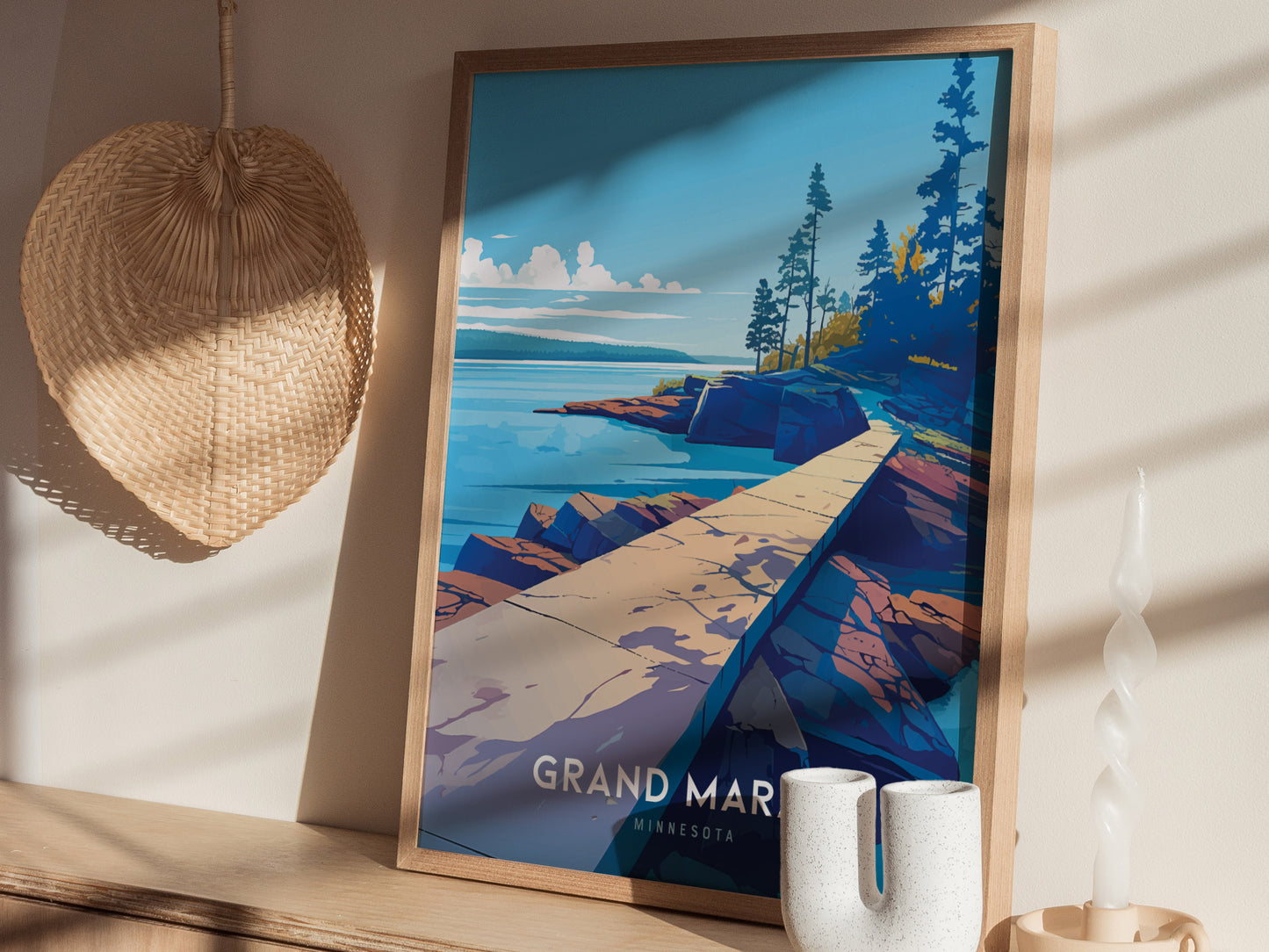 A framed poster of Grand Marais, Minnesota, featuring a scenic path along the rocky shoreline under a blue sky, is displayed on a wooden shelf with decorative items.