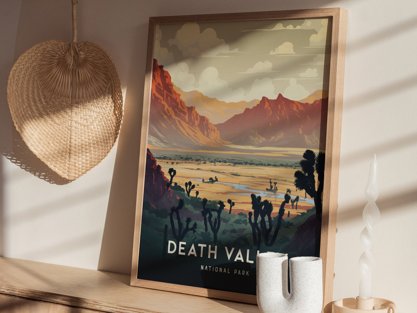 A framed print depicting Death Valleys desert landscape with mountains and Joshua trees is displayed on a shelf. A woven wall hanging and decorative candle are nearby.