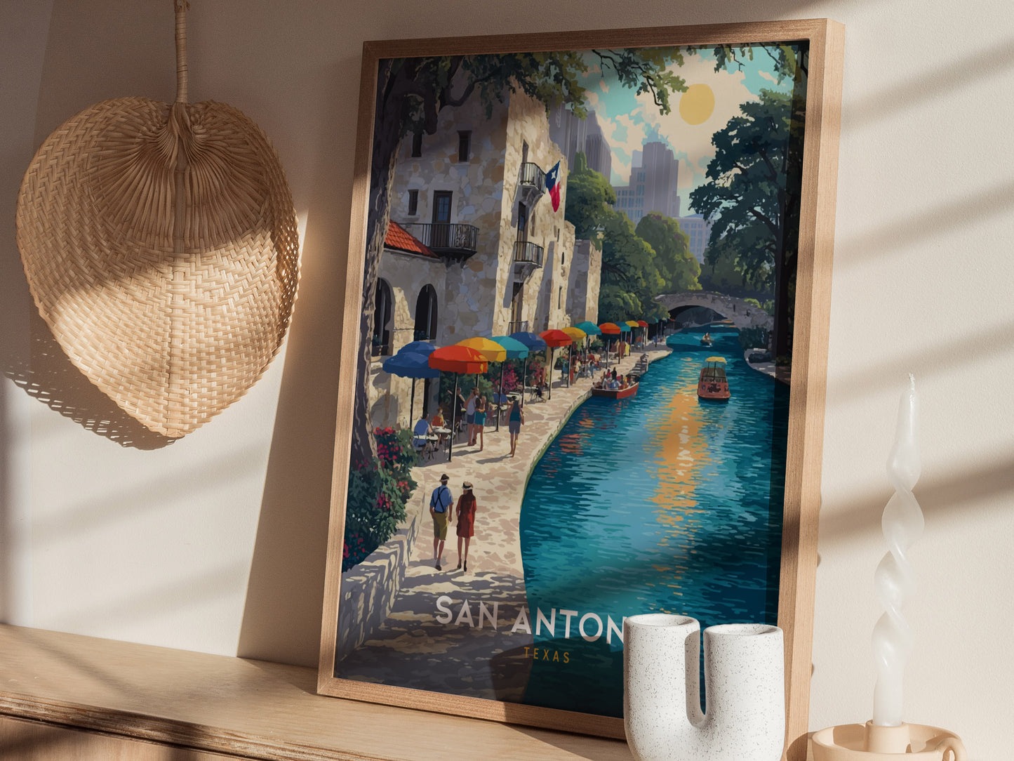 A framed poster depicting a vibrant San Antonio river scene with colorful umbrellas, boats, and a historic building. Sunlight casts shadows on the wall, with decorative items nearby.