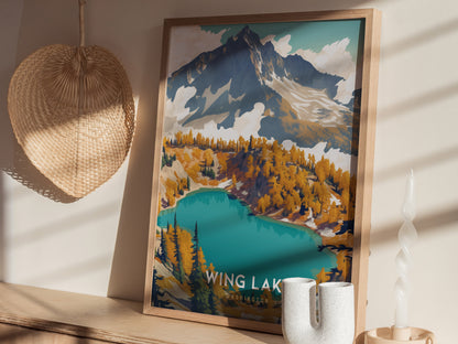 A framed poster of Wing Lake, Washington, showcasing turquoise waters and colorful trees, sits on a wooden shelf next to a woven fan and modern candle holder.