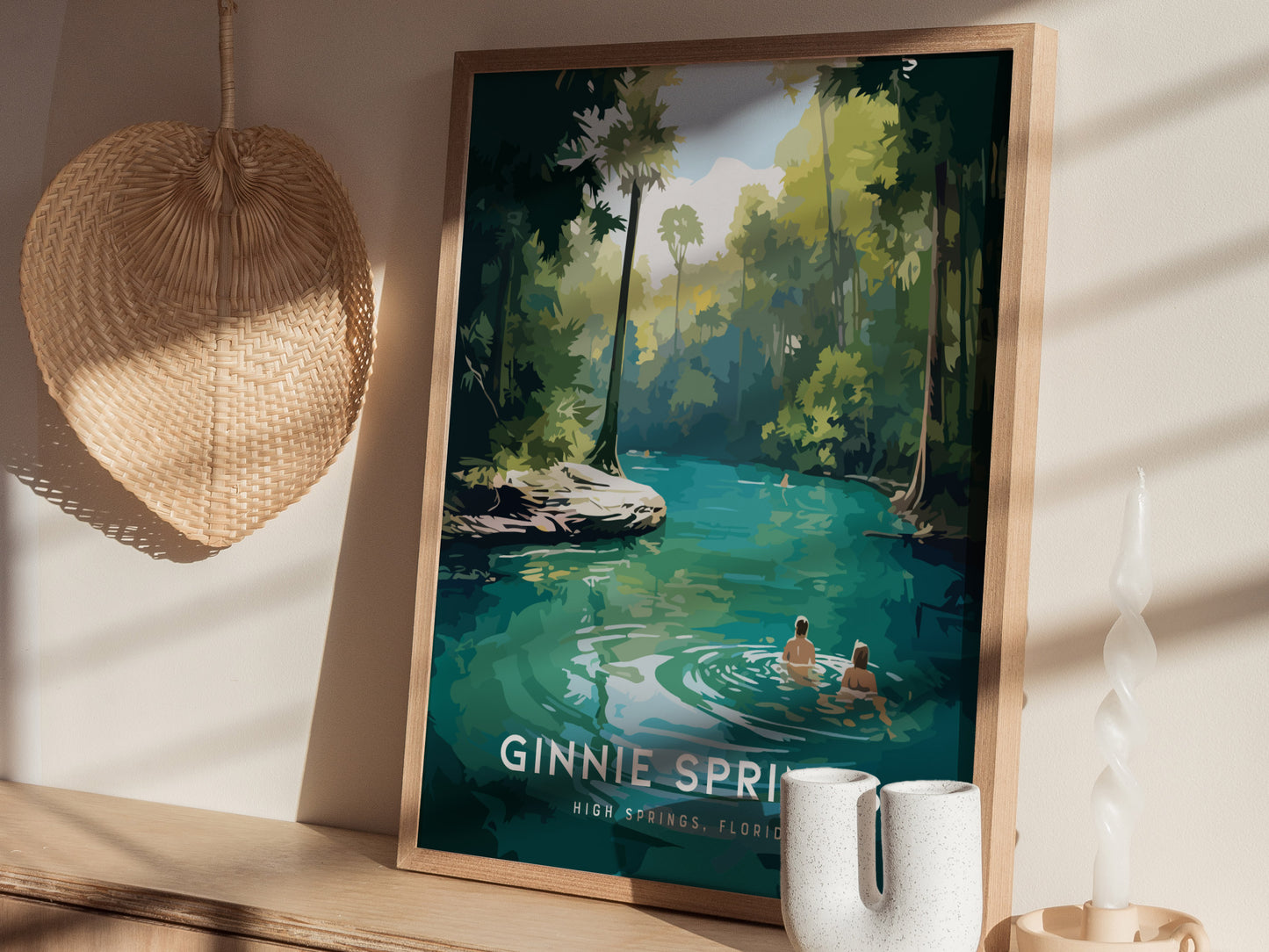A framed poster of Ginnie Springs, featuring turquoise waters and lush foliage, is displayed on a wooden shelf. A woven wall decoration and a twisted candle are nearby.