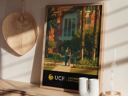 A framed poster of the University of Central Florida campus sits on a shelf, next to a woven fan and a decorative candle. Sunlight casts shadows on the wall.