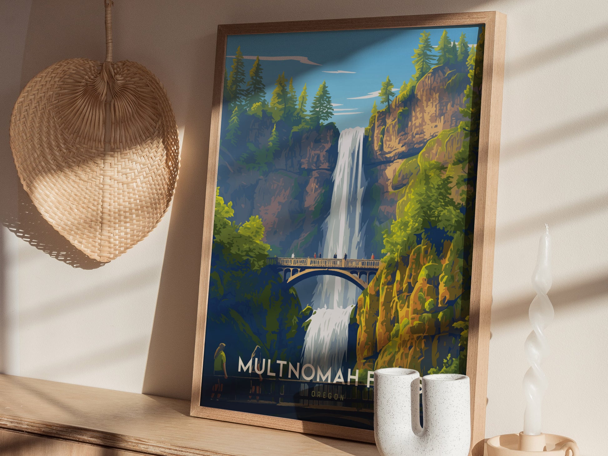 Framed Multnomah Falls poster featuring the waterfall, Benson Bridge, and lush cliffs, displayed on a shelf with a decorative woven item and ceramic vases. Sunlight casts shadows on the wall.