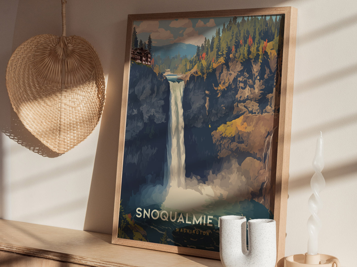 A framed poster of Snoqualmie Falls is displayed on a wooden shelf, alongside a woven wall decor and a uniquely shaped white candle.