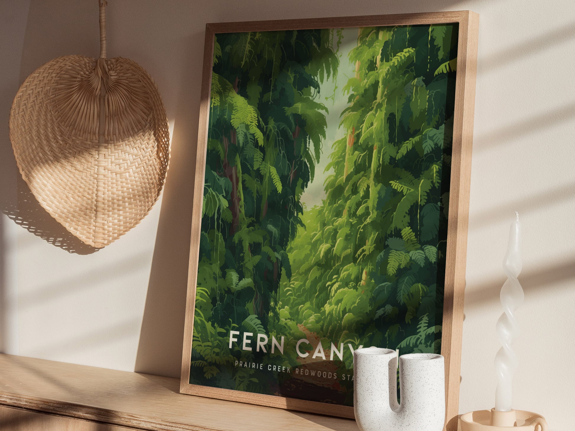 A framed poster depicting lush green ferns in a canyon setting is displayed on a shelf with a woven wall decoration and a twisted candle nearby.