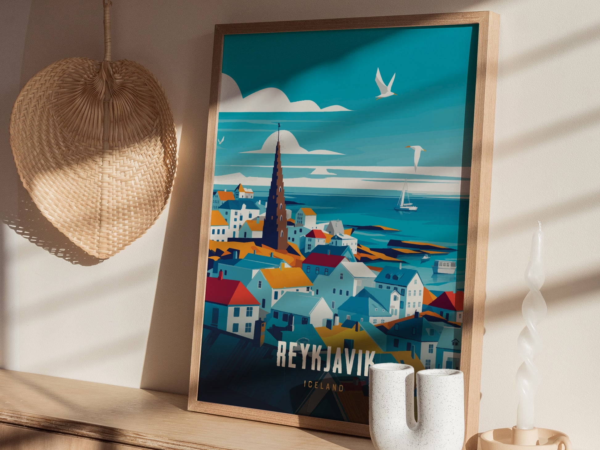 A framed travel poster of Reykjavík, Iceland features colorful houses and a tall spire under a blue sky. It rests on a shelf with a wicker basket and candle nearby.