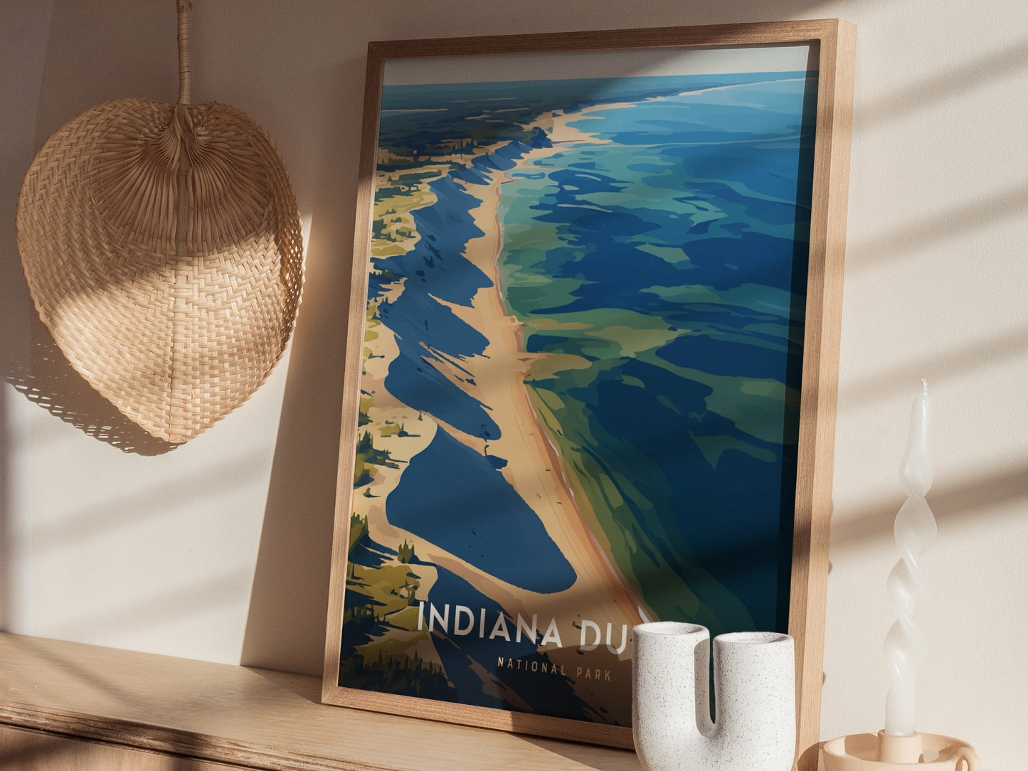 A framed poster of Indiana Dunes National Park featuring a stylized view of the shoreline is displayed on a wooden surface, next to a woven decorative piece and a twisted.