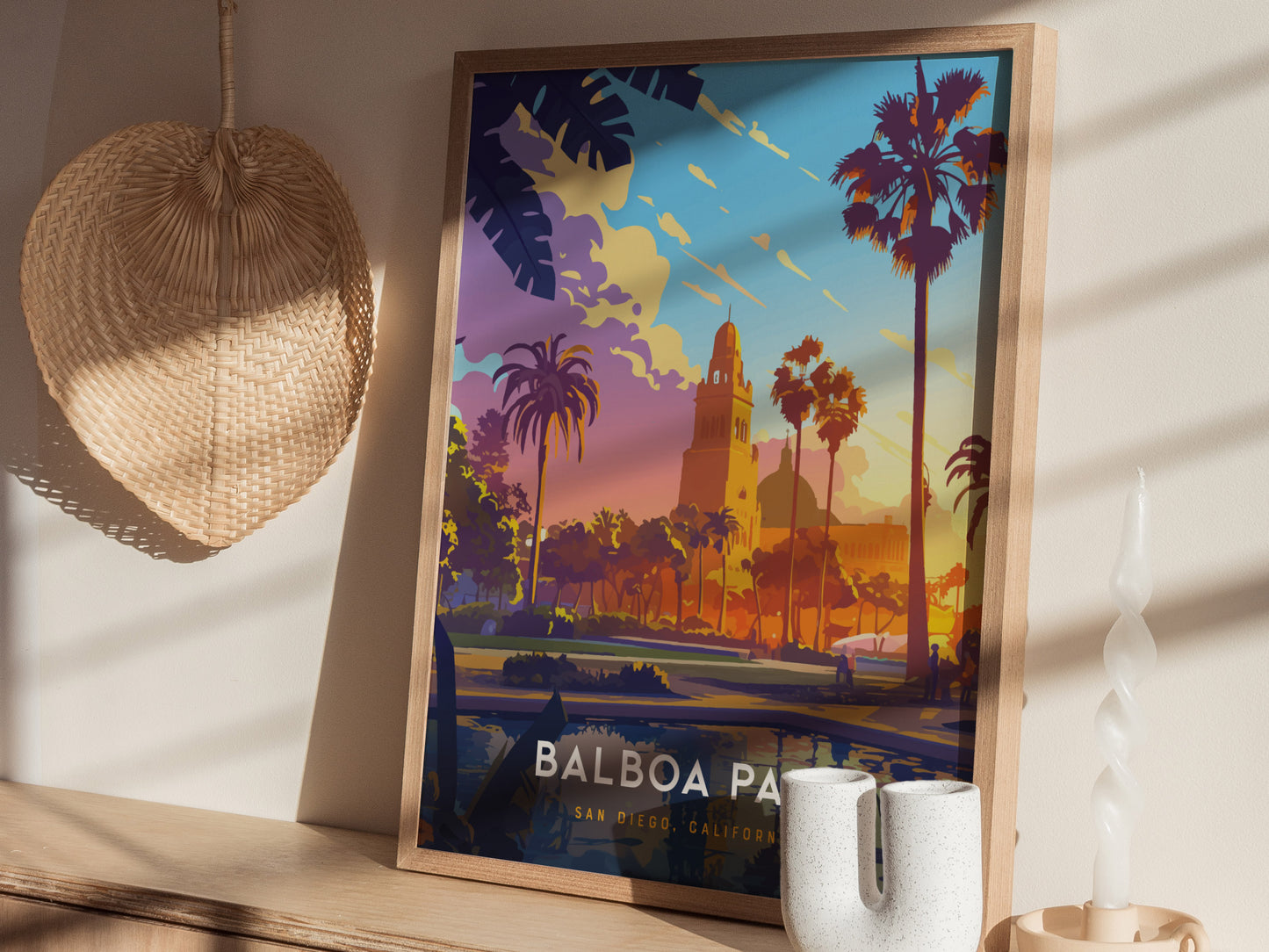 A framed Balboa Park poster with colorful palm trees and architecture sits on a wooden shelf, accompanied by a wicker fan and decorative items.