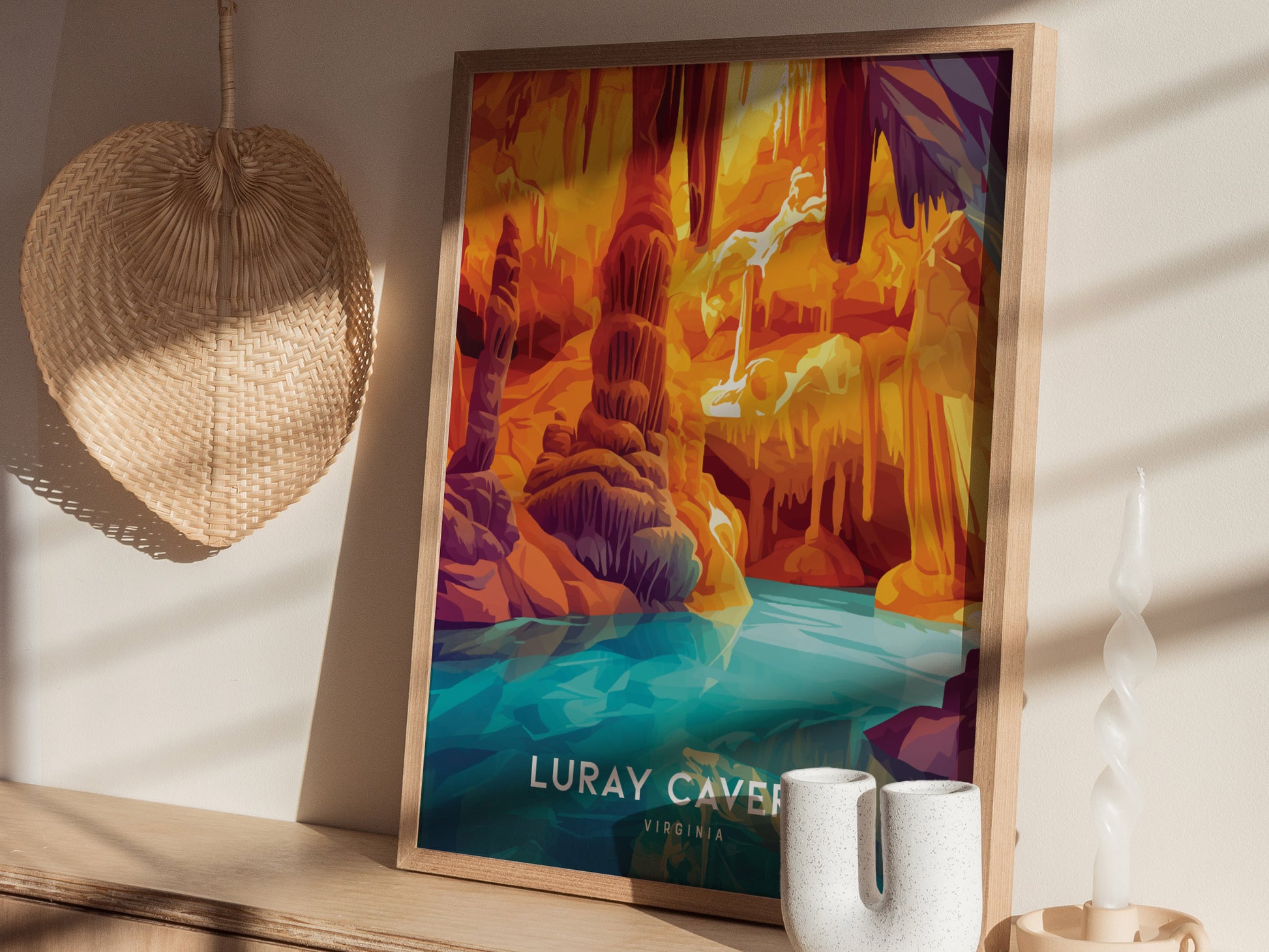 Framed Luray Caverns poster featuring vibrant orange and purple rock formations above a blue pool, displayed on a wooden shelf with a woven fan and decorative candle nearby.