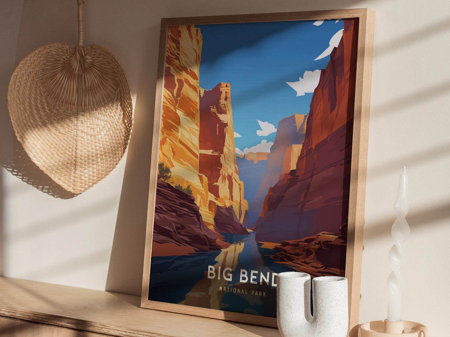 A framed poster of Big Bend National Park features dramatic canyon cliffs and a clear blue sky, displayed on a shelf with a woven basket and a twisted candle.