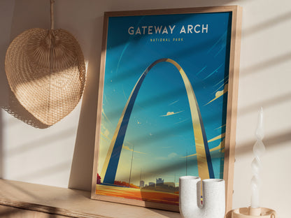 A framed poster of the Gateway Arch in St. Louis, Missouri, leans against a wall with a blue sky backdrop. Nearby, a woven fan and decorative candle are visible.