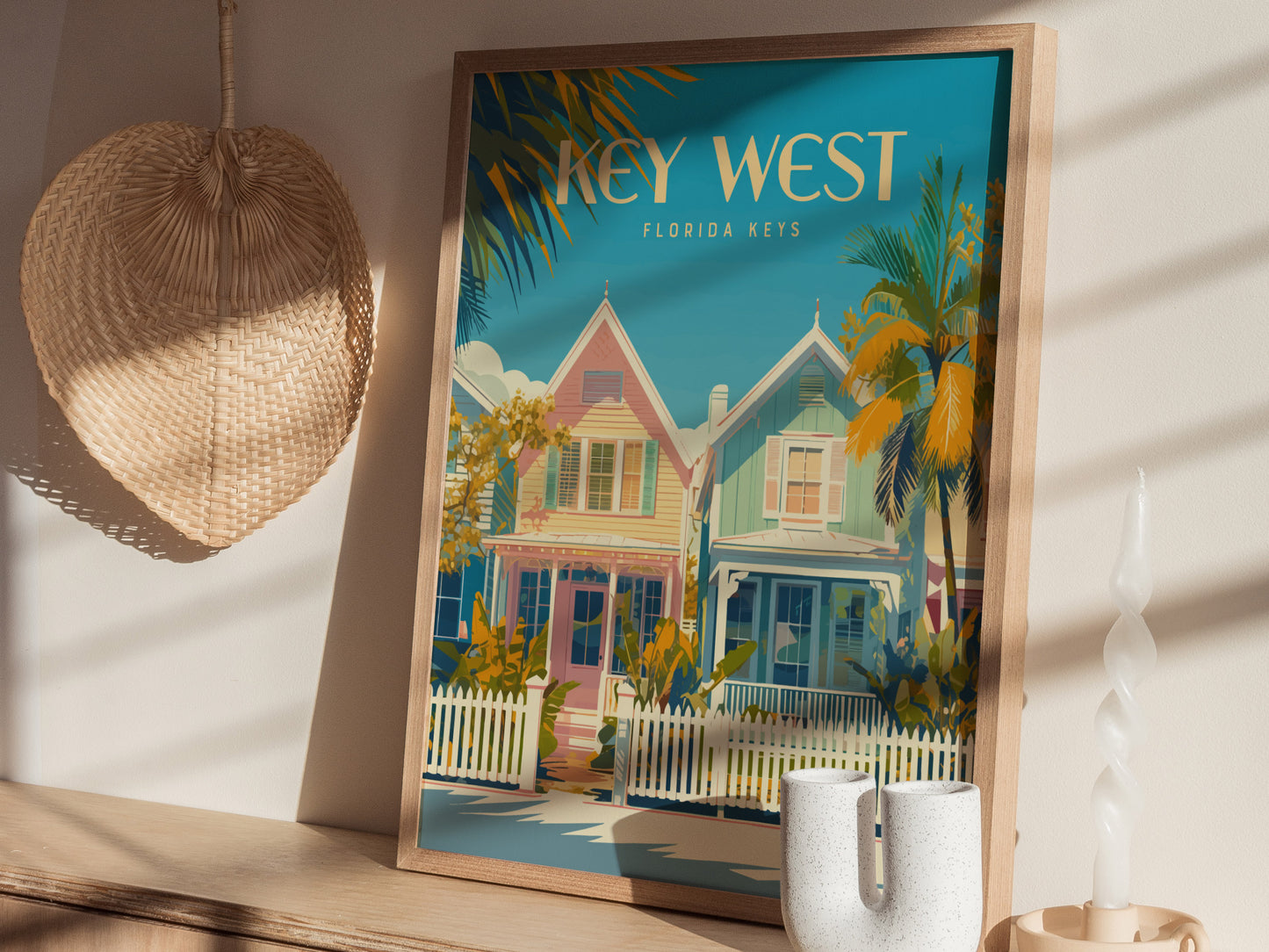 A framed Key West poster featuring colorful houses and palm trees is displayed on a wooden surface. Nearby, a woven basket.