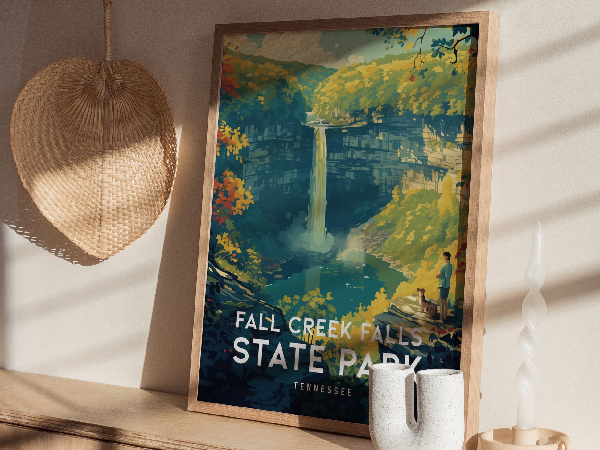A framed Fall Creek Falls poster leans against a wall, depicting a hiker and dog overlooking a waterfall surrounded by vibrant autumn foliage.