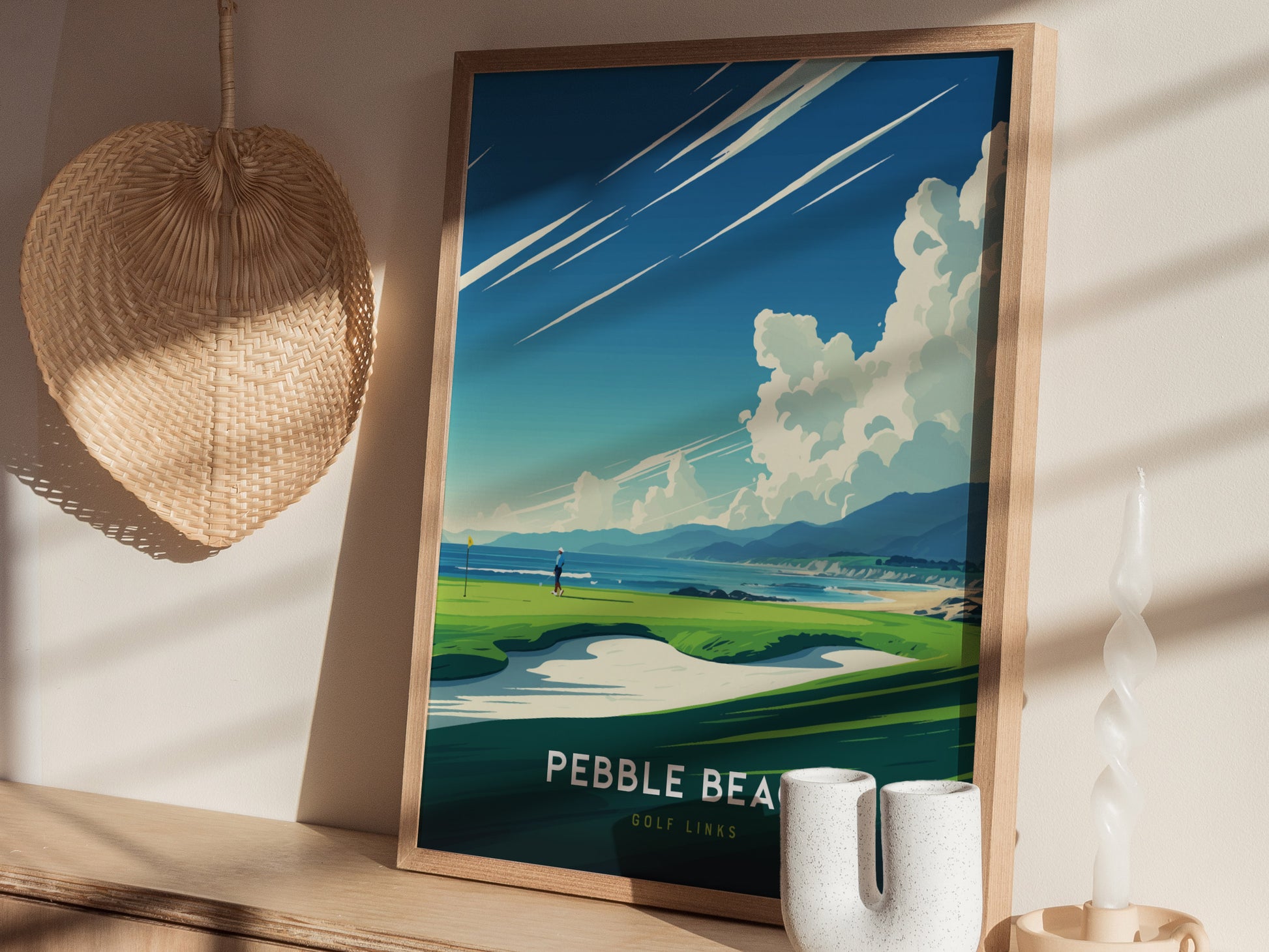 A framed poster of Pebble Beach Golf Links features a vibrant coastal scene under a dramatic sky. It rests on a shelf beside a woven wall decoration and a twisted.