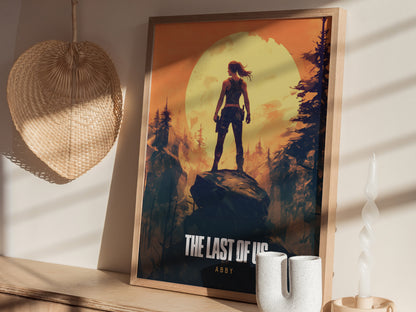 Framed poster featuring a silhouetted figure standing on a rock against a large yellow sun and forest background. Its displayed on a wooden surface alongside a woven basket and candle.