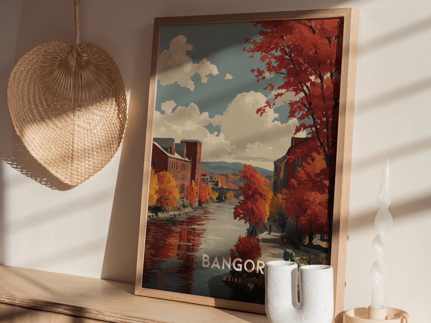 A framed artwork featuring a picturesque autumn scene of Bangor, showcasing vibrant orange and red trees along a calm river.