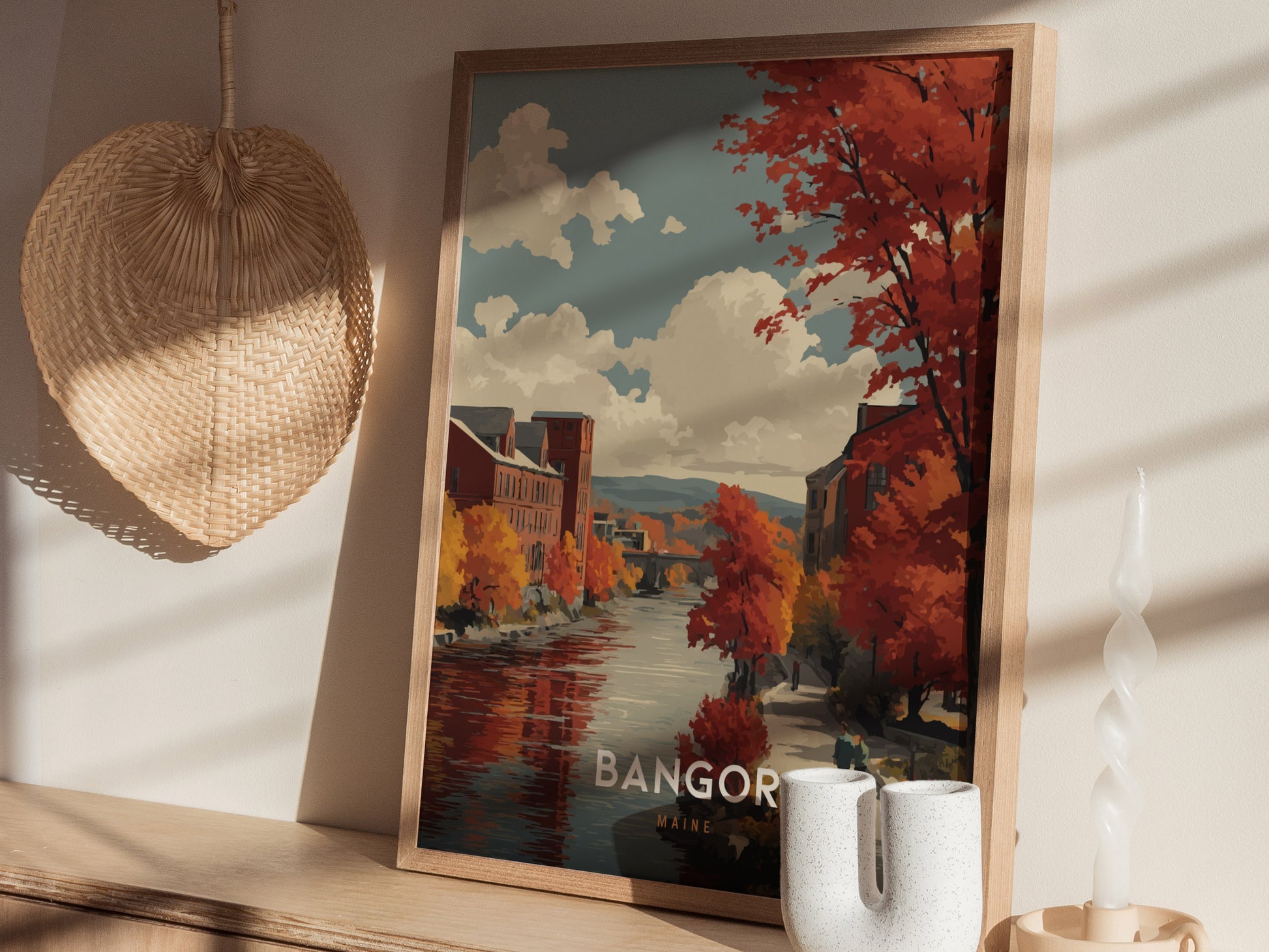 A framed artwork featuring a picturesque autumn scene of Bangor, showcasing vibrant orange and red trees along a calm river.