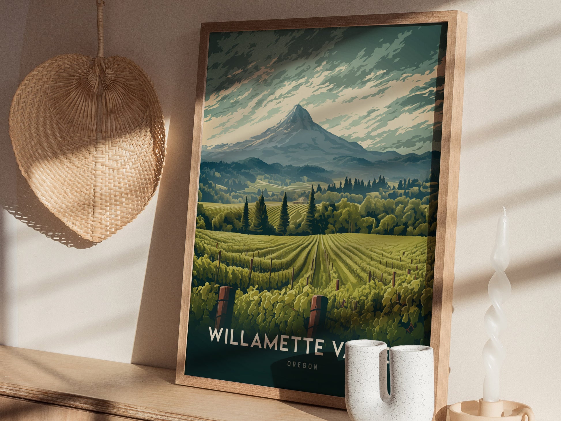 Framed artwork of Willamette Valley in Oregon, featuring lush vineyards and a distant mountain, sits on a shelf beside a woven fan and decorative candle.