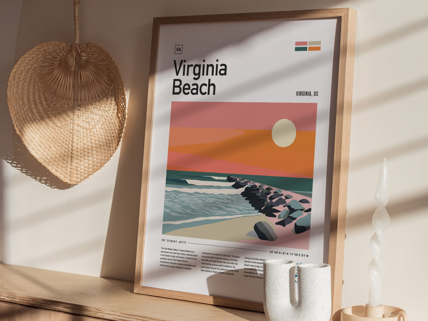 A framed poster of Virginia Beach featuring a stylized sunset and jetty is displayed on a wooden shelf, accompanied by a woven fan and a twisted candle.