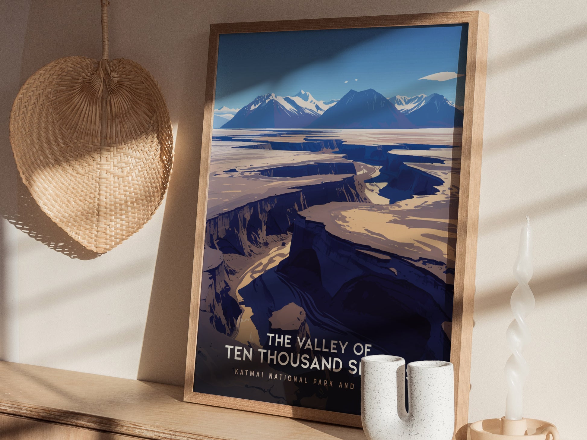 A framed poster of The Valley of Ten Thousand Smokes on a wooden shelf, accompanied by a woven basket and decorative candle, with shadows cast on the wall.