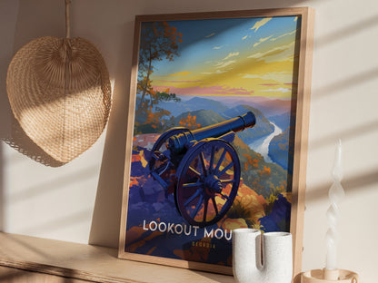 A framed poster depicting a cannon overlooking a scenic mountain landscape at sunset, set against a wall with a woven basket and decorative items nearby.
