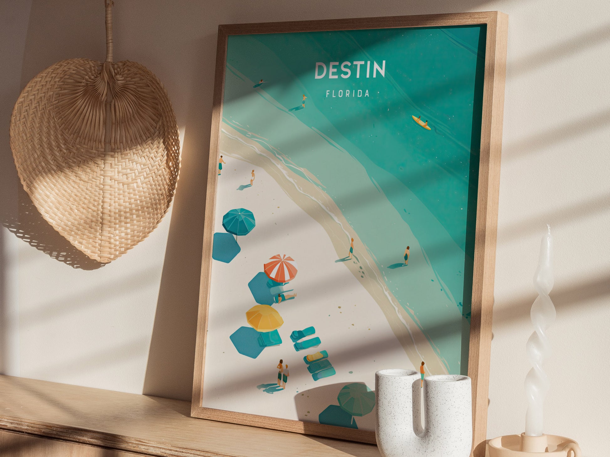 A framed Destin, Florida poster featuring a beach scene with turquoise waters and colorful umbrellas is displayed on a shelf next to a woven wall decoration and a white candle.