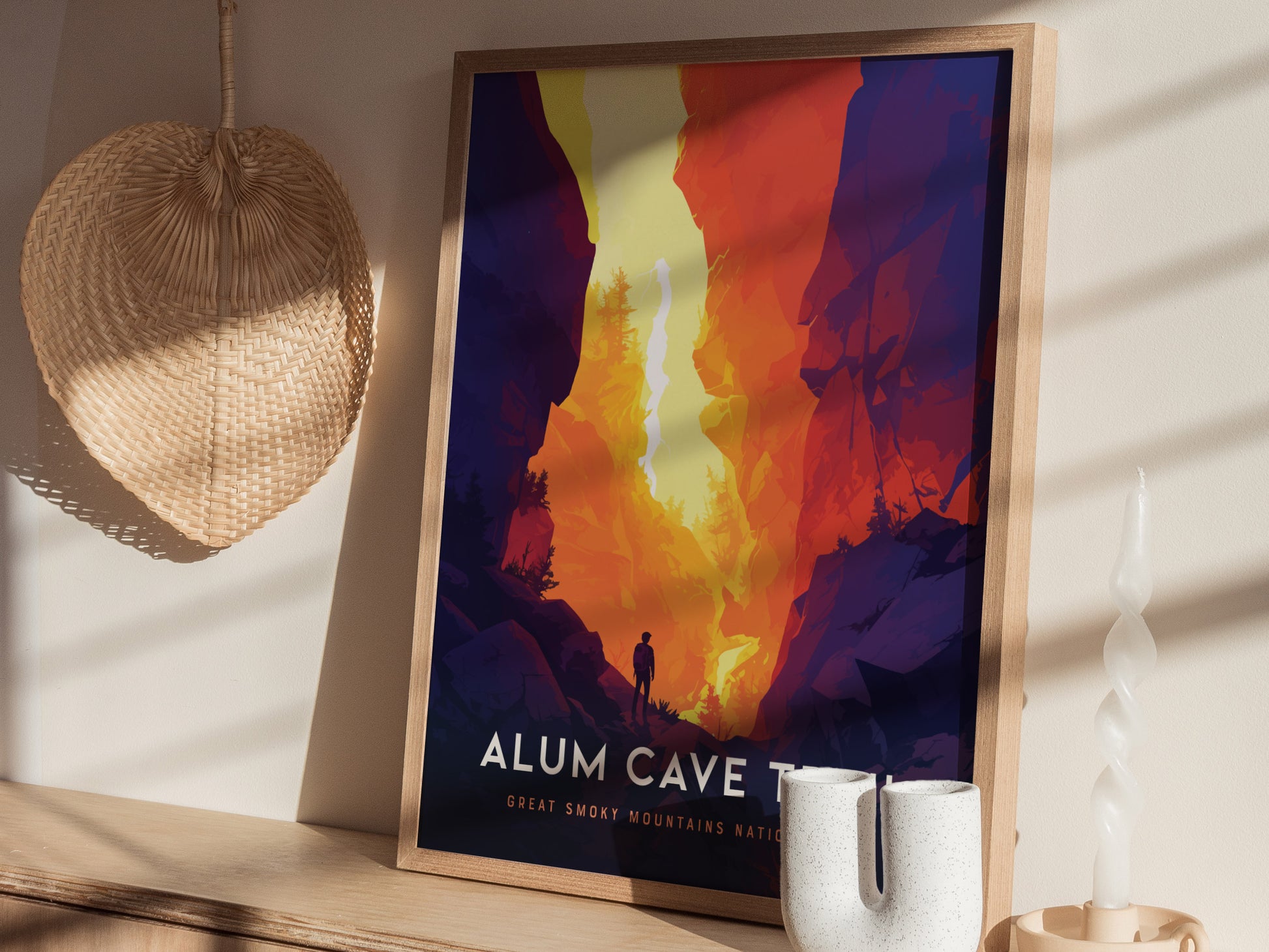 A colorful poster of Alum Cave Trail featuring a silhouette of a hiker amidst vibrant cliffs is framed and placed on a shelf, beside a woven basket and a twisted.